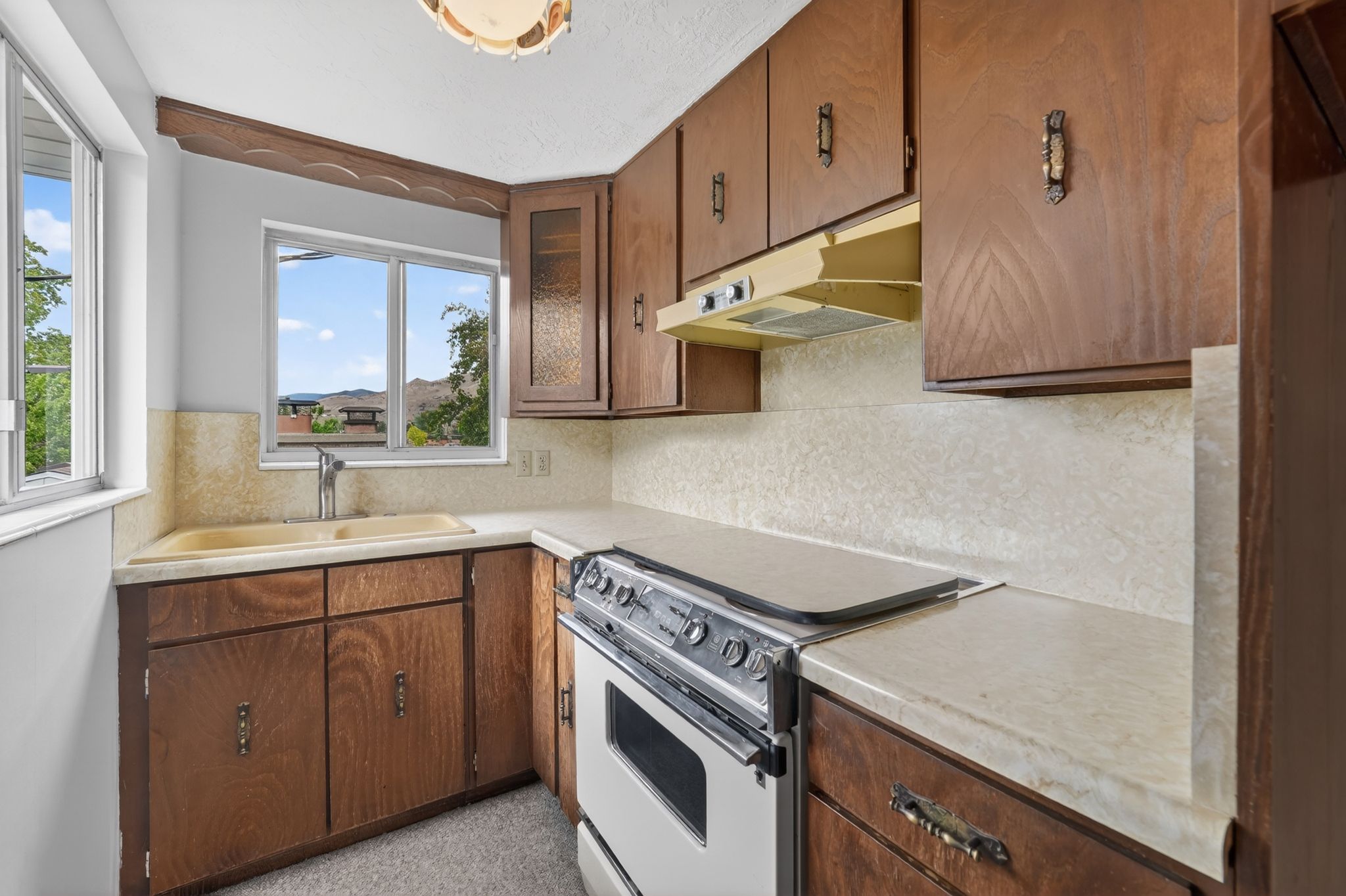 Kitchen featuring wood-finish cabinetry, a double basin sink, and a four-burner range with an overhead vent