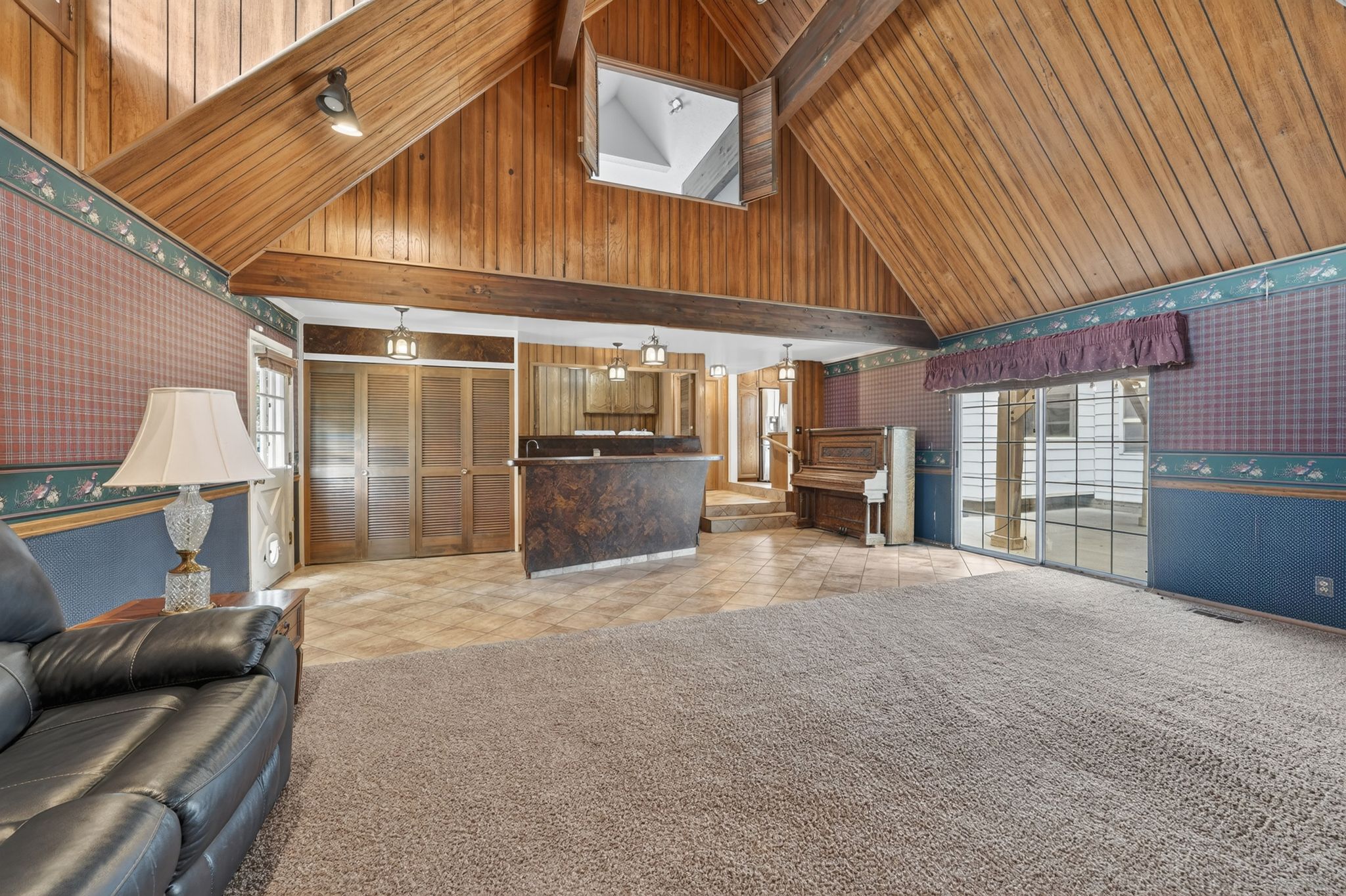Vaulted wood-paneled ceiling with exposed beams, textured carpet flooring, tiled flooring, built-in bar, and sliding glass doors