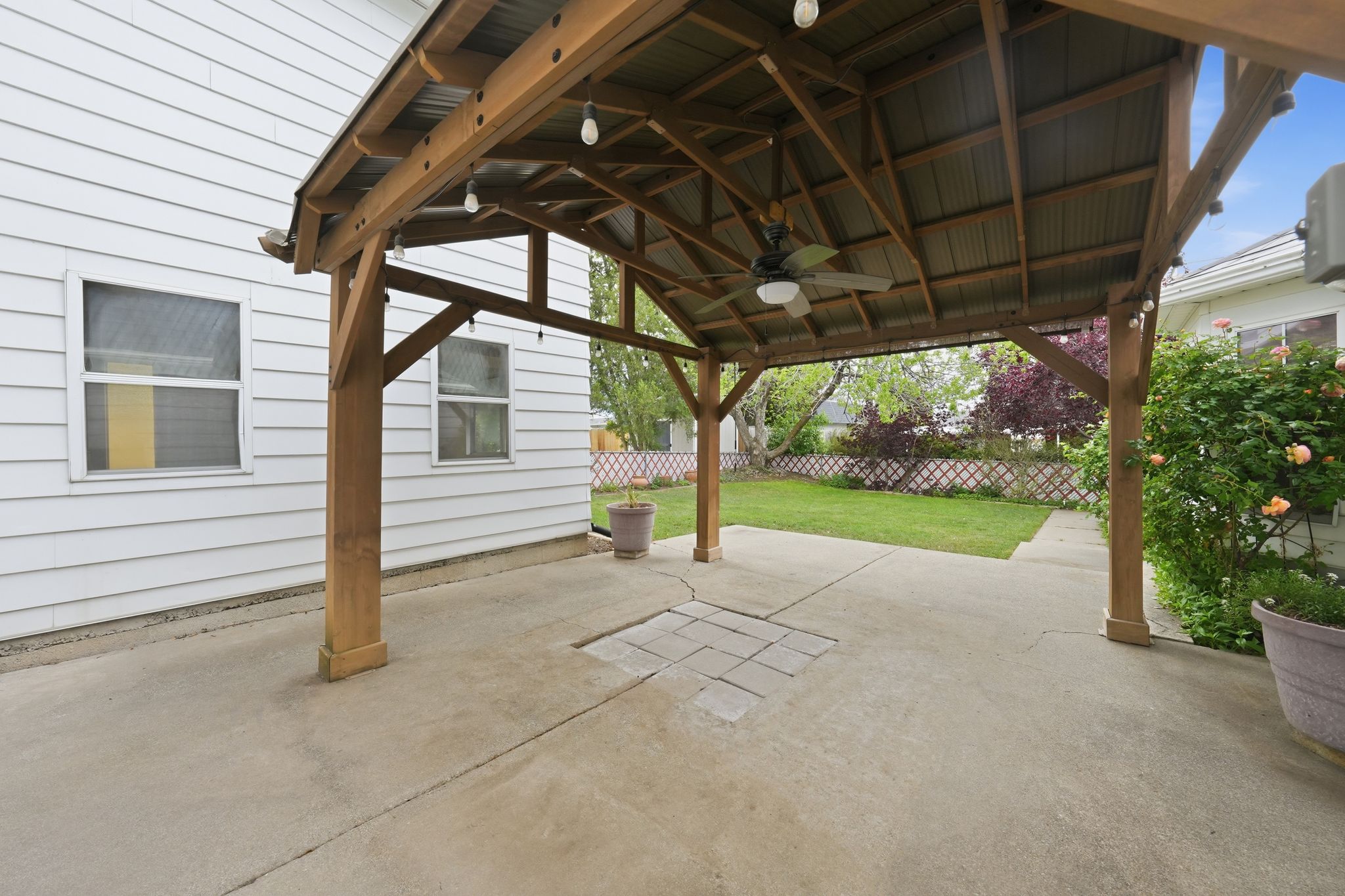 Covered patio featuring a wood-frame structure with a metal roof, integrated ceiling fan, and string lighting