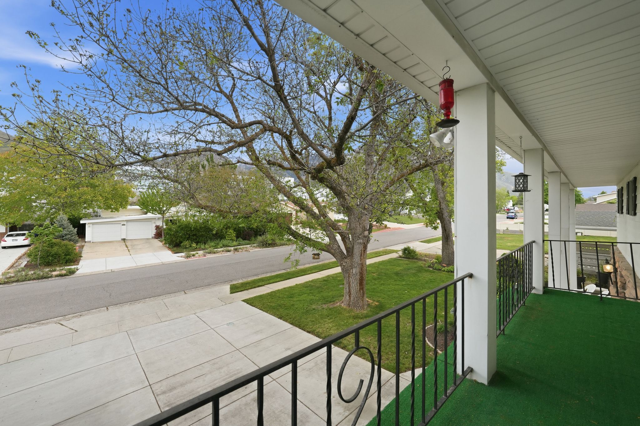 Covered front porch featuring a black wrought iron railing, white support columns, and green outdoor carpeting