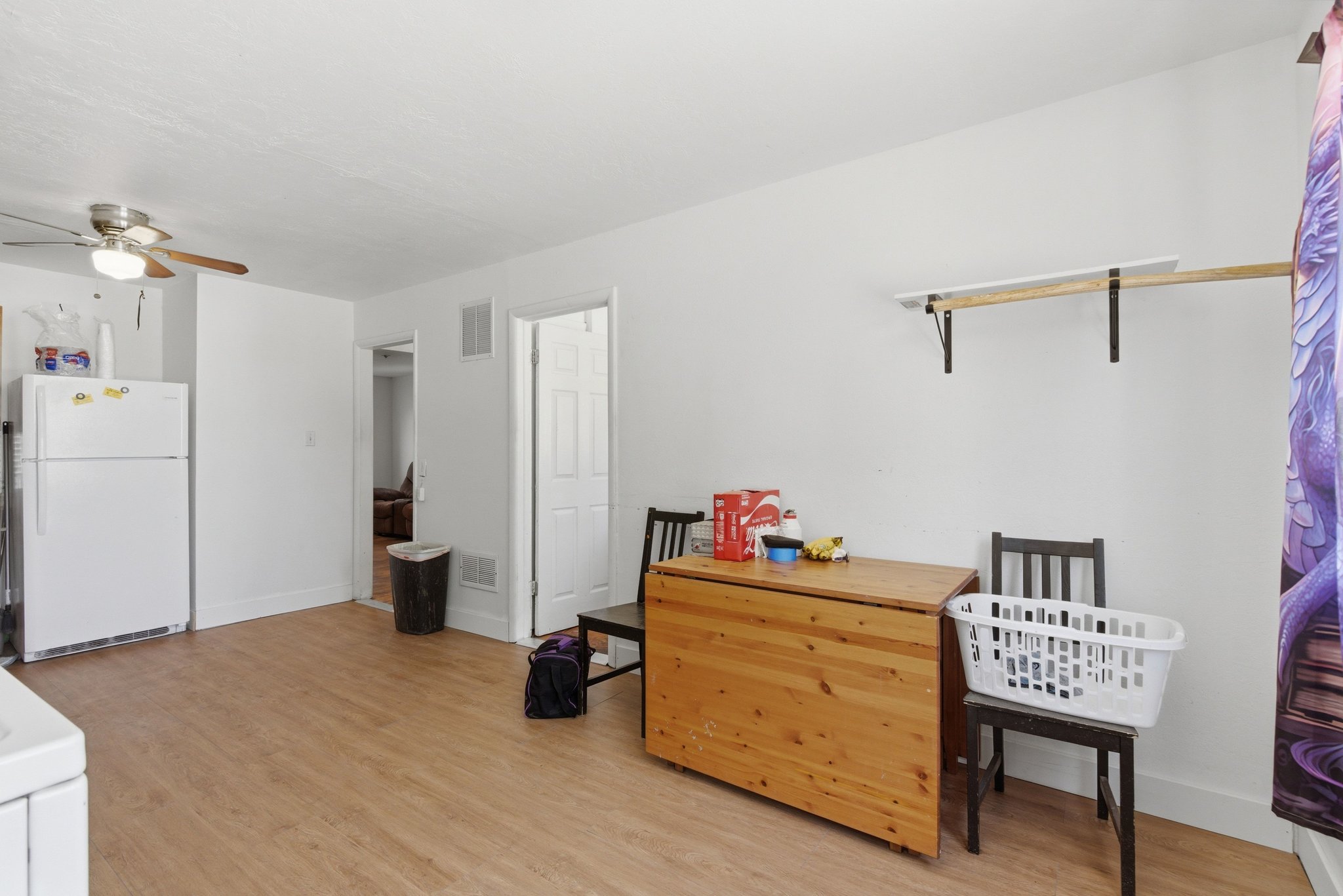 Open-concept living area featuring wood-finish flooring, white walls, and a ceiling fan with integrated lighting