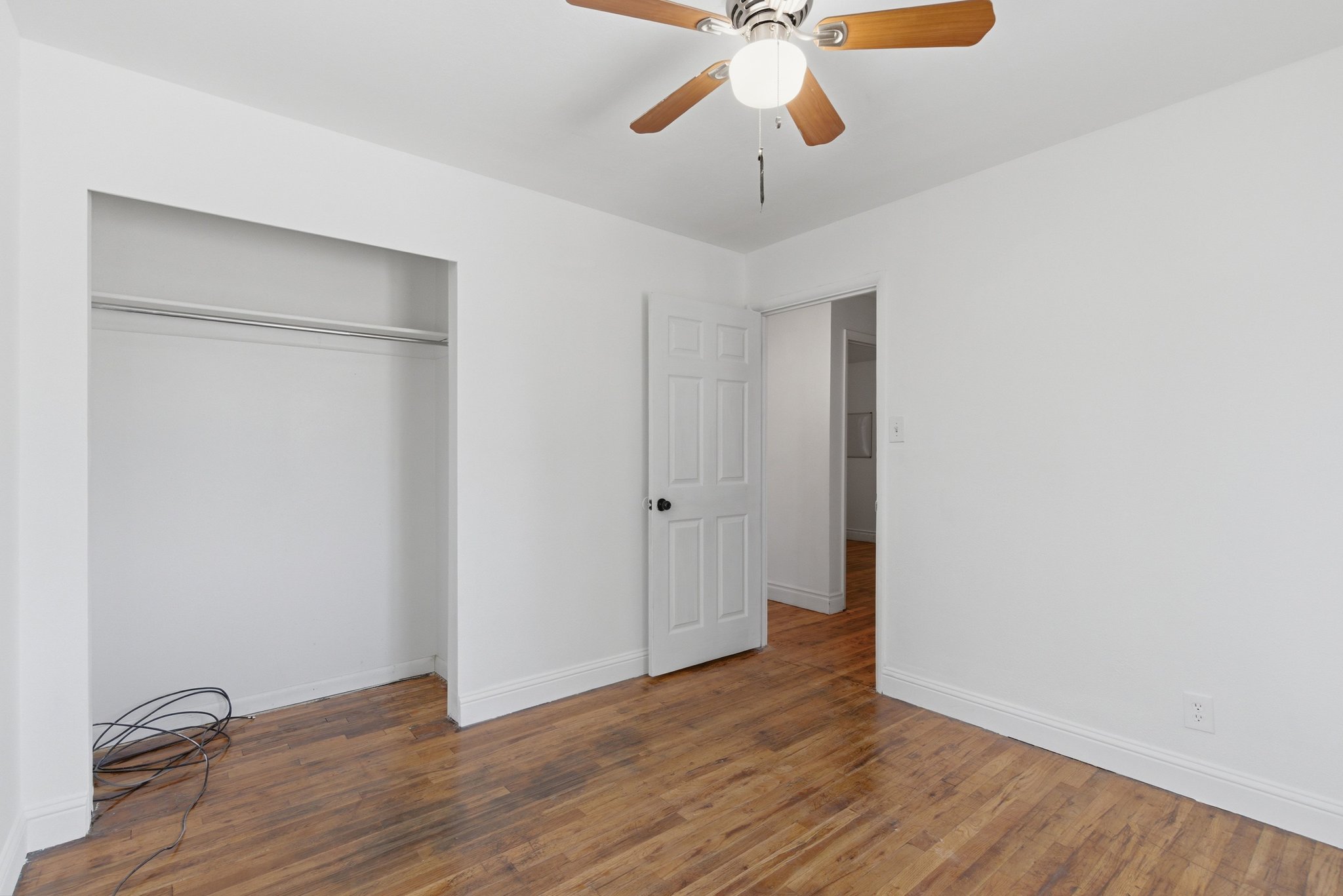 Room featuring wood-finish flooring, a ceiling fan with integrated lighting, a paneled door, and an open closet with a hanging rod