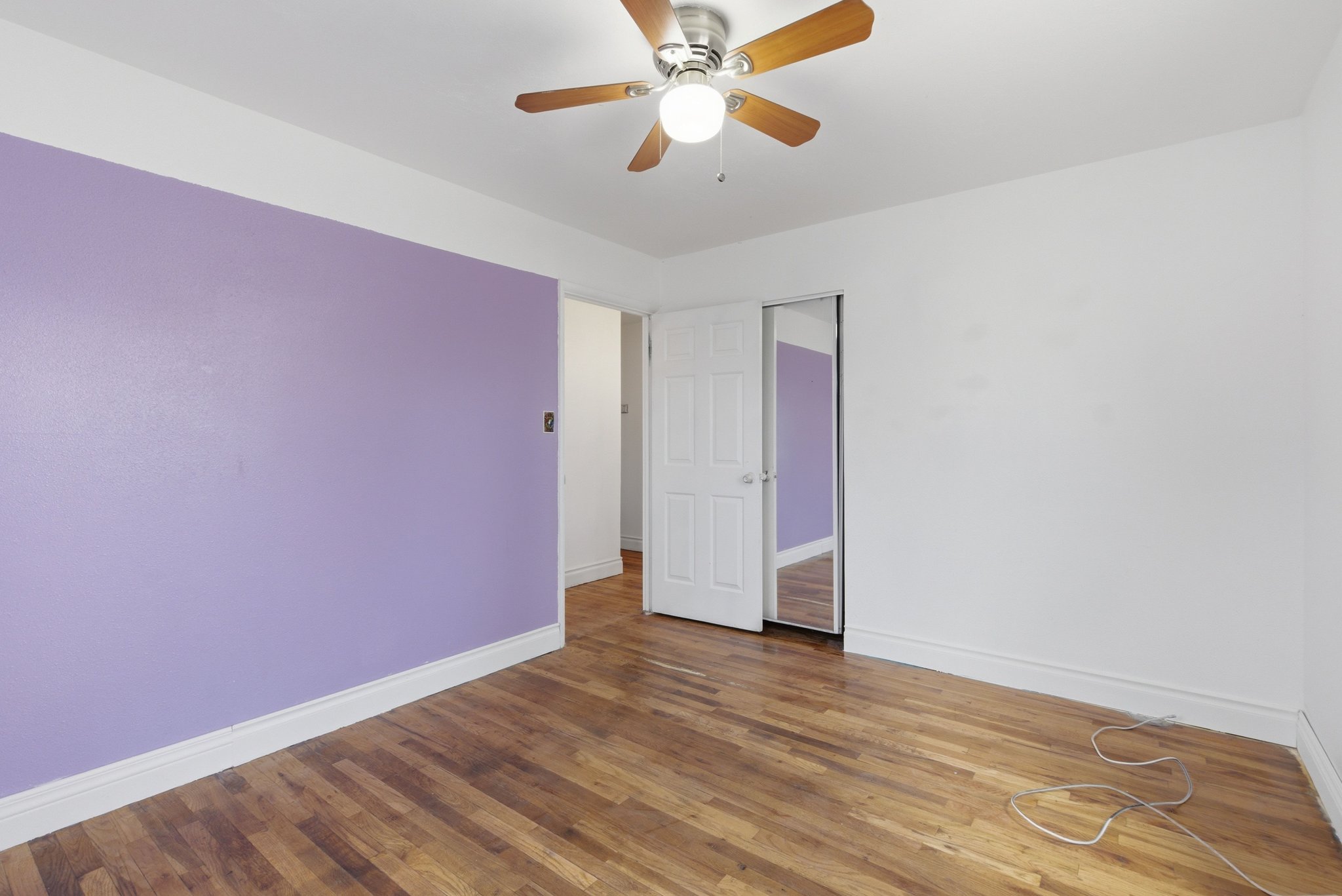 Room featuring wood-finish flooring, a ceiling fan with light fixture, and a white baseboard trim