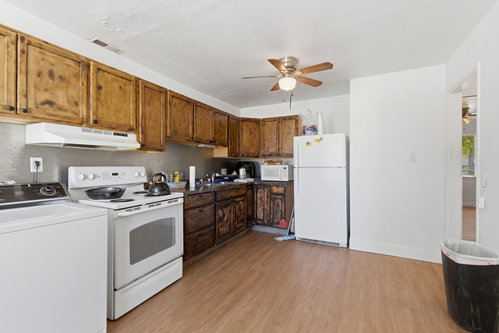 Kitchen featuring wood-finish cabinetry, white appliances including a range and refrigerator, a ceiling fan, and wood-finish flooring