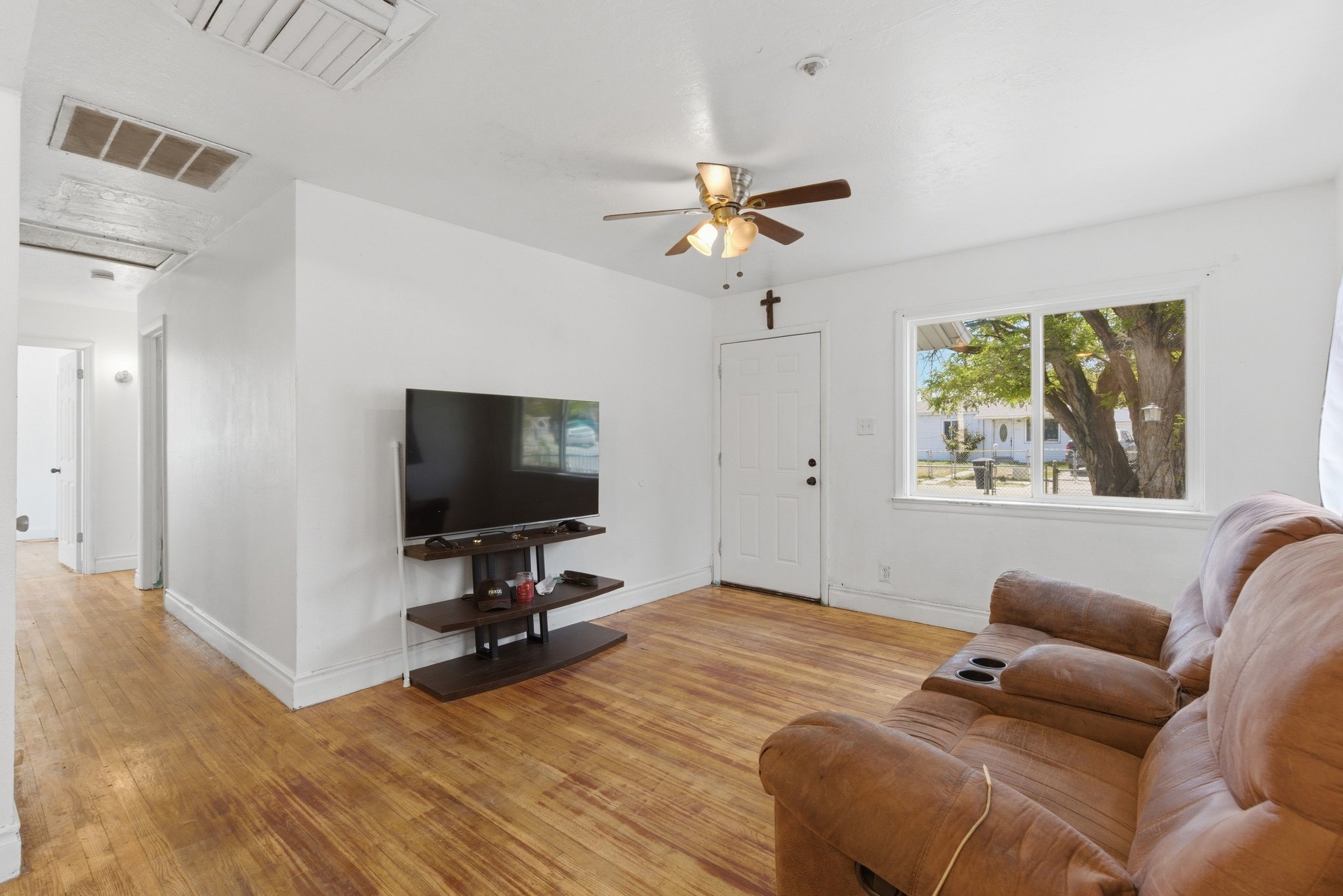 Living area featuring wood-finish flooring, a white paneled entrance door, and a ceiling fan with integrated lighting
