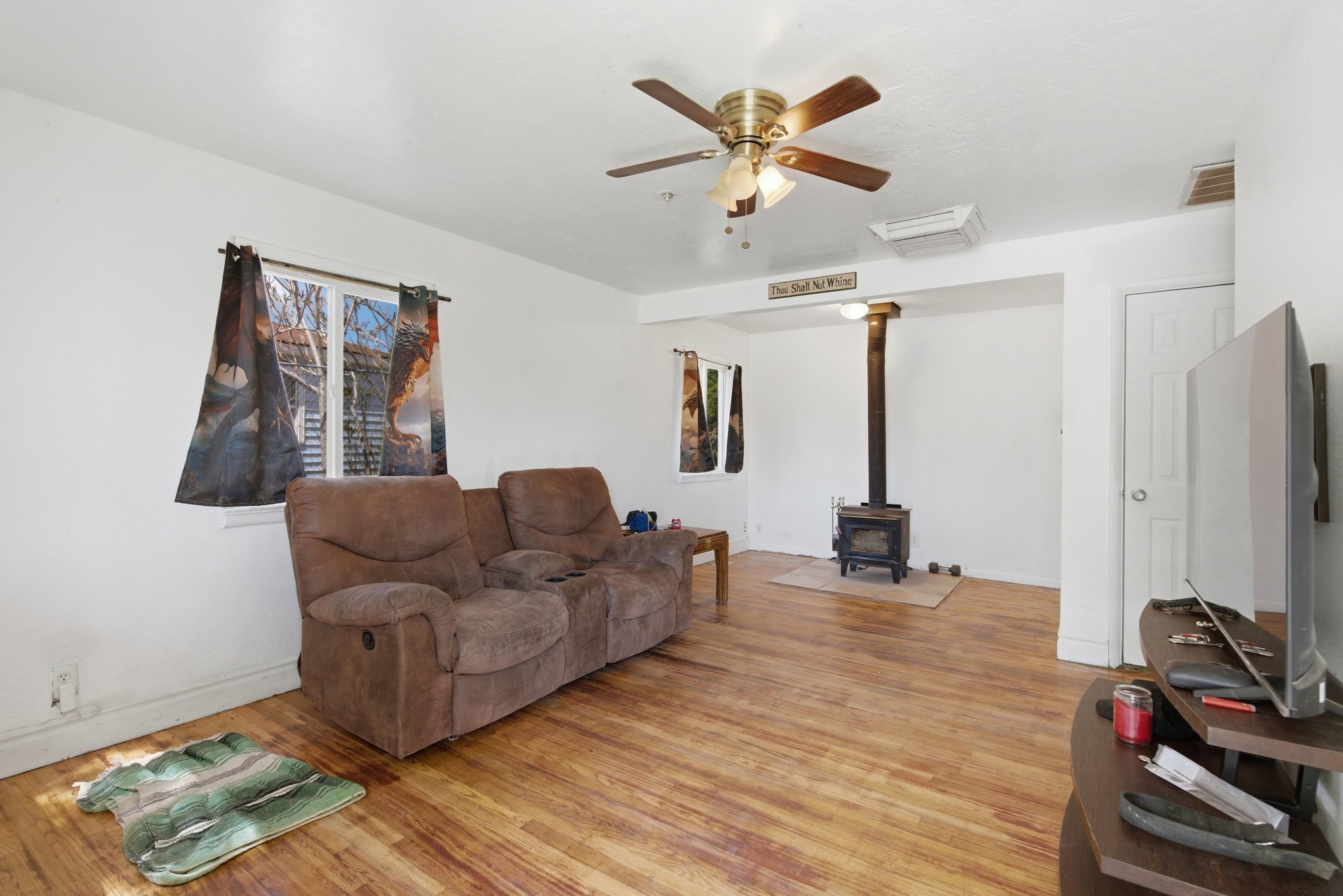 Living area featuring wood-finish flooring, a ceiling fan with integrated lighting, and a freestanding wood-burning stove on a tiled hearth