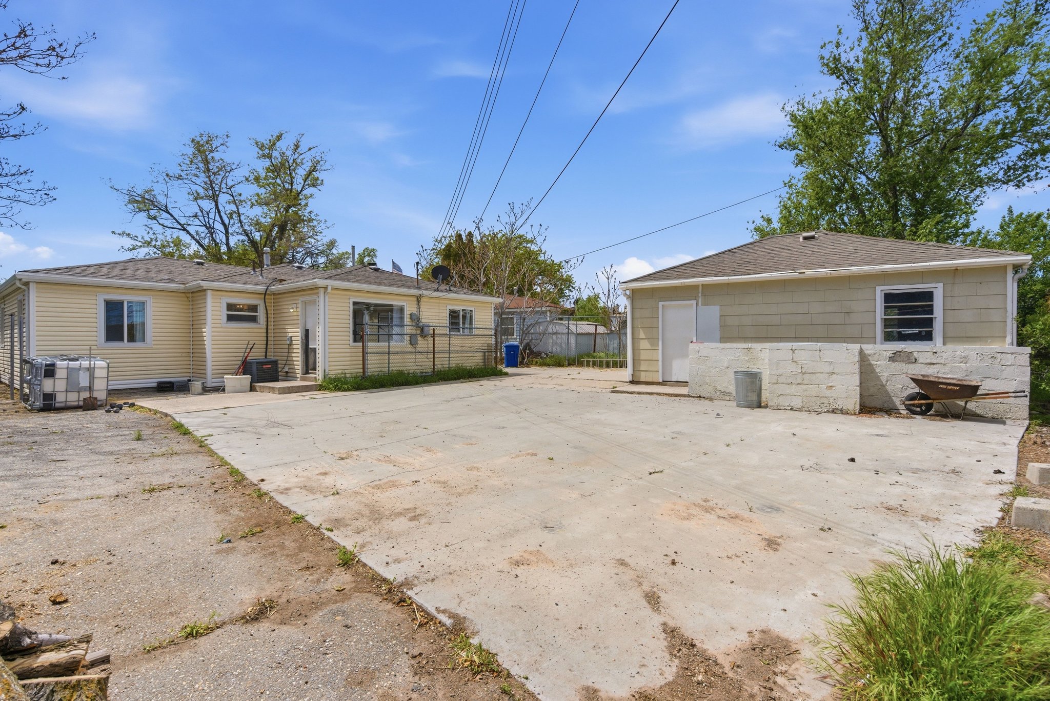 Spacious concrete yard featuring a detached building, a primary residence with siding, and mature trees