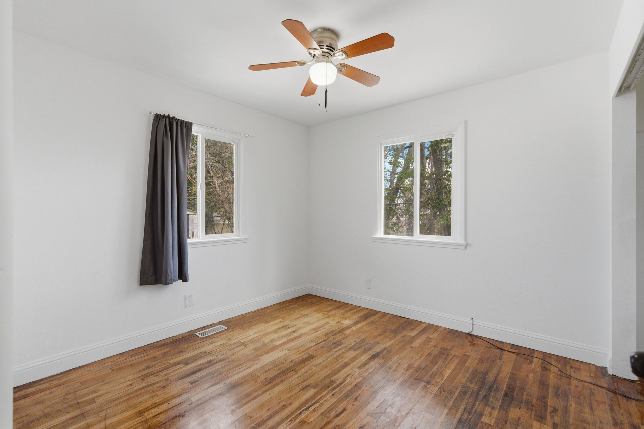Bright interior space featuring wood-finish flooring, white baseboards, and two windows with white trim