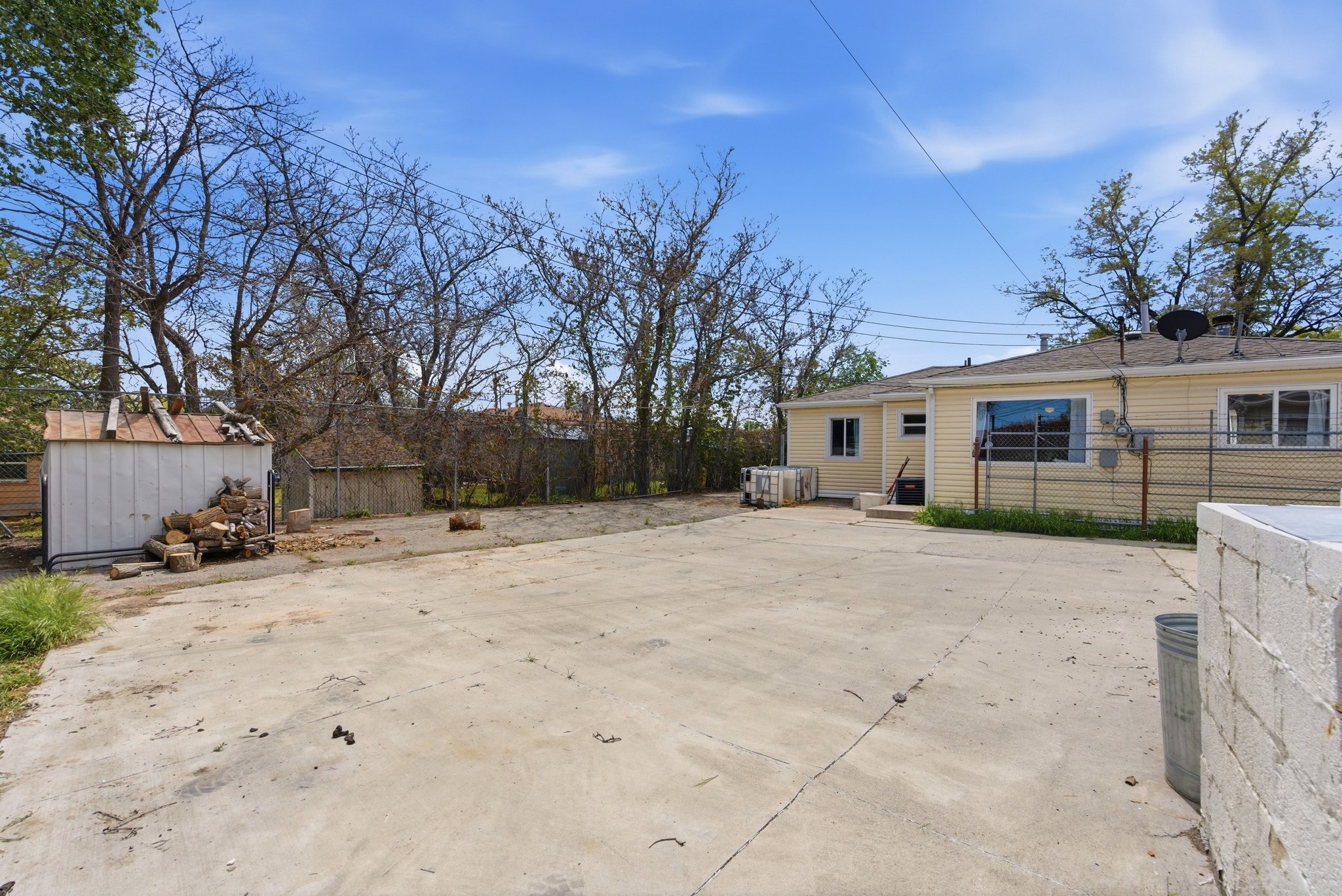 Expansive concrete patio area with a detached storage shed and a single-story residence featuring horizontal siding and multiple windows