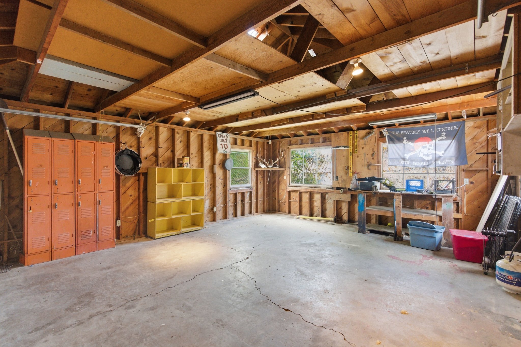 Spacious garage featuring exposed wood framing, concrete flooring, overhead lighting, and two windows providing natural light