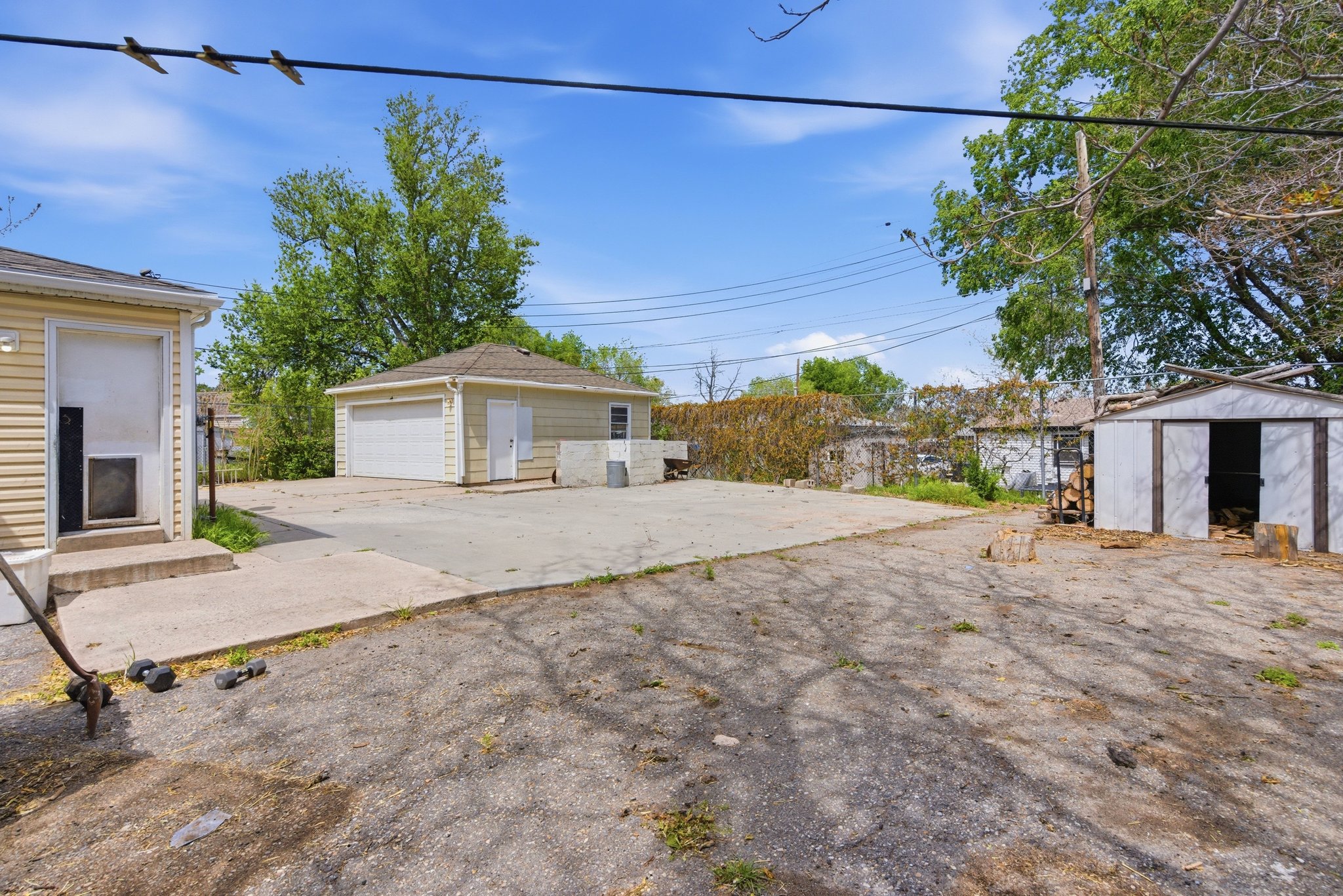 Expansive paved area providing ample parking, featuring a detached two-car garage with a roll-up door, an additional storage shed with a single entry, and a building with horizontal siding