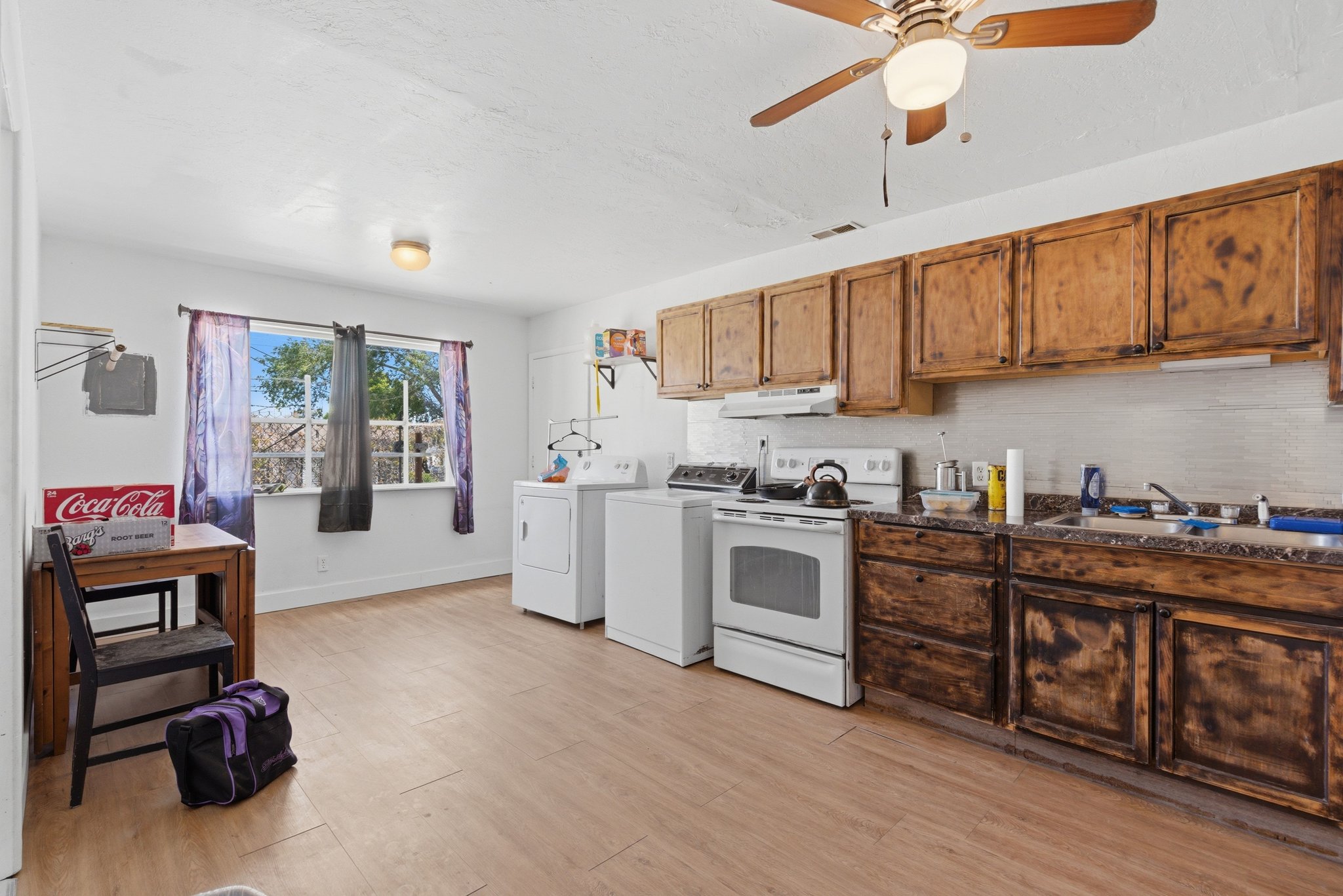 Spacious room featuring wood-finish flooring, a full kitchen with dark wood-finish cabinetry, white appliances, and a double basin sink
