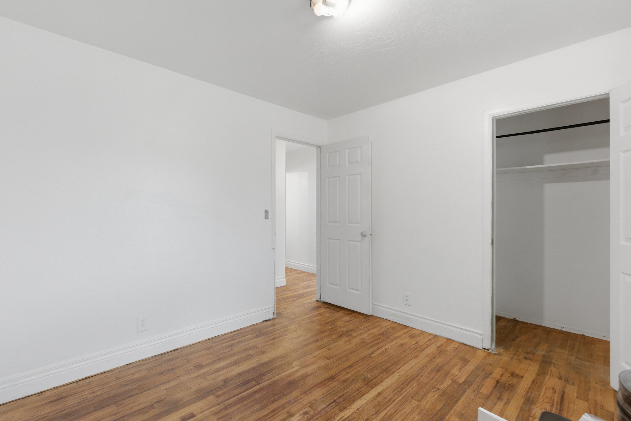 Spacious room featuring wood-finish flooring, white painted walls, and a built-in closet with shelving