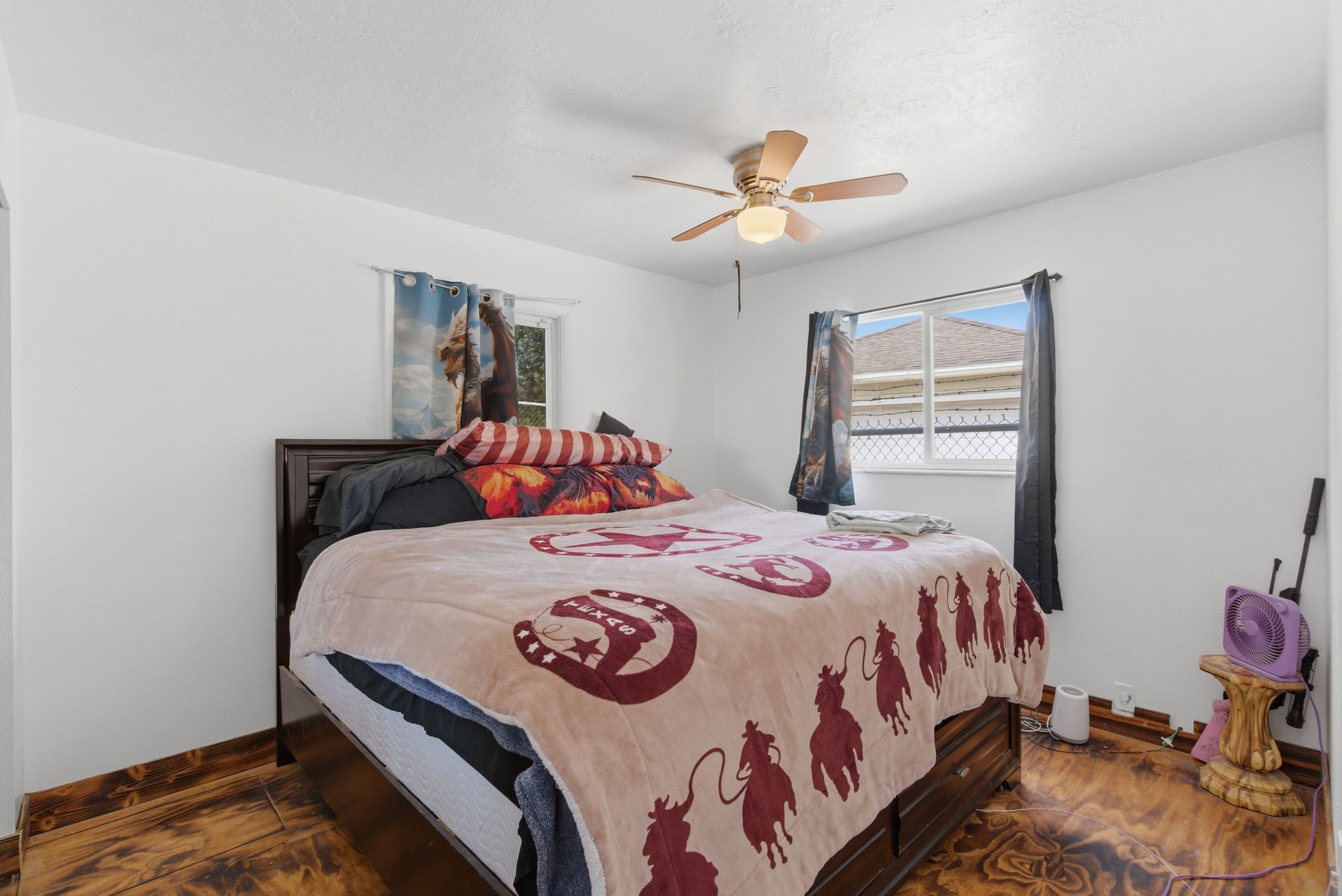 Bedroom featuring unique wood-finish flooring, white walls, and two windows providing natural light