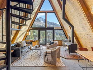 Living area with a high wood beamed ceiling, a wood stove, wooden walls, a mountain view, and carpet flooring