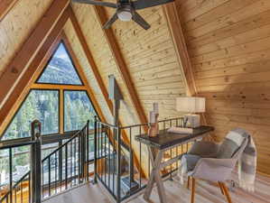 Additional living space with a wooden ceiling with exposed beams, light wood-style floors, ceiling fan, and wooden walls