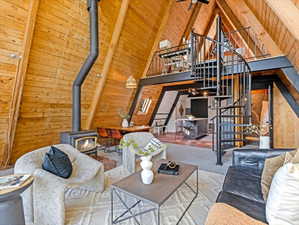 Living area with wooden walls, a wood stove, a high wood beamed ceiling, and carpet floors