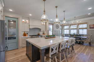 Spacious kitchen featuring a large central island with seating, pendant lighting, stainless steel appliances, and wood-finish flooring