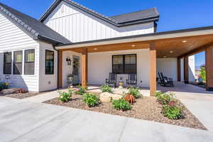 White exterior with dark trim windows, covered porch, wood-finish ceiling, and low-maintenance landscaping