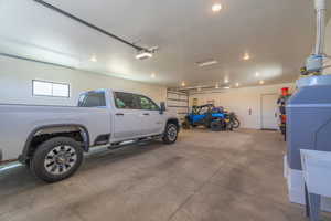 Spacious garage with exposed concrete flooring, two overhead garage doors, ample recessed lighting, and a utility sink