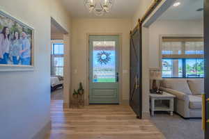 Entryway featuring wood-finish flooring, a light green front door with decorative glass, a prominent barn door with brass hardware, and a beaded chandelier