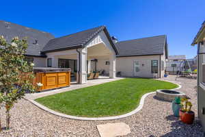 Expansive backyard featuring a covered patio, built-in fire pit, manicured lawn, and natural stone gravel landscaping