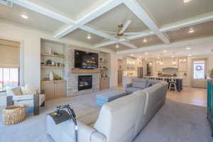Spacious living area featuring a coffered ceiling with recessed lighting and a ceiling fan, a stone-faced fireplace with a wood mantel, and built-in shelving and cabinetry