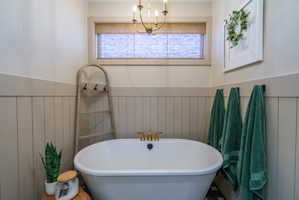 Freestanding soaking tub with brass fixtures, board and batten wainscoting, and a window with a woven shade