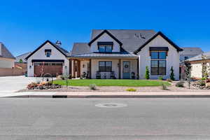 Modern farmhouse exterior featuring white vertical siding, black trim, a covered front porch with wood columns, an attached garage with a wood-finish door, and a manicured front lawn with xeriscaping