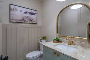 Bathroom featuring wainscoting, an arched gold-framed mirror, a light-toned countertop, an undermount sink, and a gold-finish faucet