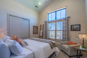 Vaulted ceiling bedroom featuring a large window with transom, neutral paint colors, and plush carpet flooring