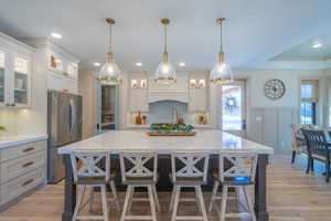 Spacious kitchen featuring a large central island with seating, stainless steel refrigerator, light wood-finish flooring, white cabinetry, and recessed lighting