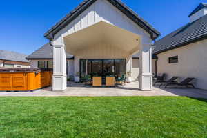 Expansive green lawn with a covered patio, featuring a built-in outdoor spa, a large sliding glass door, and tiled roofing
