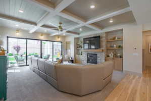 Spacious living area featuring a coffered ceiling with recessed lighting and a ceiling fan, a stone-faced fireplace with a wood mantel, built-in shelving, and large multi-panel glass sliding doors opening to an outdoor area