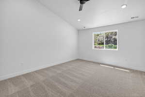 Spacious room featuring neutral carpeting, white walls, and a modern ceiling fan