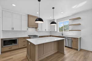 Modern kitchen featuring an island with a quartz countertop, two-tone cabinetry, stainless steel appliances, and wood-finish flooring