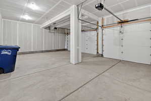 Spacious garage with concrete flooring, two white garage doors, and exposed ceiling joists