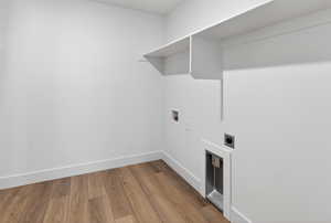 Dedicated laundry space featuring wood-finish flooring, white walls, built-in shelving, and utility hookups