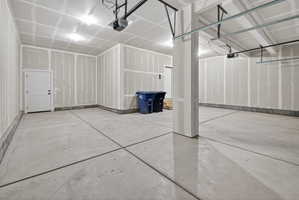 Spacious garage featuring a concrete floor, overhead lighting, and an interior access door