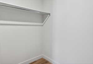 Closet interior featuring a chrome hanging rod, white shelving, and wood-finish flooring