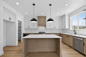 Modern kitchen featuring a central island with a light-toned countertop, two-tone cabinetry with white upper and wood-finish lower cabinets, a white subway tile backsplash, and wood-finish flooring
