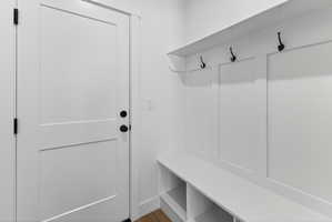 Built-in white mudroom bench featuring cubby storage, upper shelving, and three black coat hooks