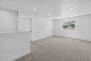 Spacious room featuring neutral carpet flooring, recessed ceiling lighting, a contemporary door, and a bright window with exterior scenery