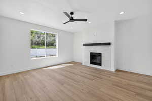 Spacious room featuring wood-finish flooring, a modern fireplace with a white tile surround and dark mantel, a contemporary ceiling fan, and recessed lighting