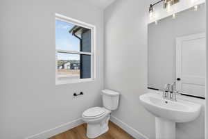 Bathroom featuring wood-finish flooring, a white pedestal sink with chrome faucet, a rectangular mirror, and a three-light vanity fixture