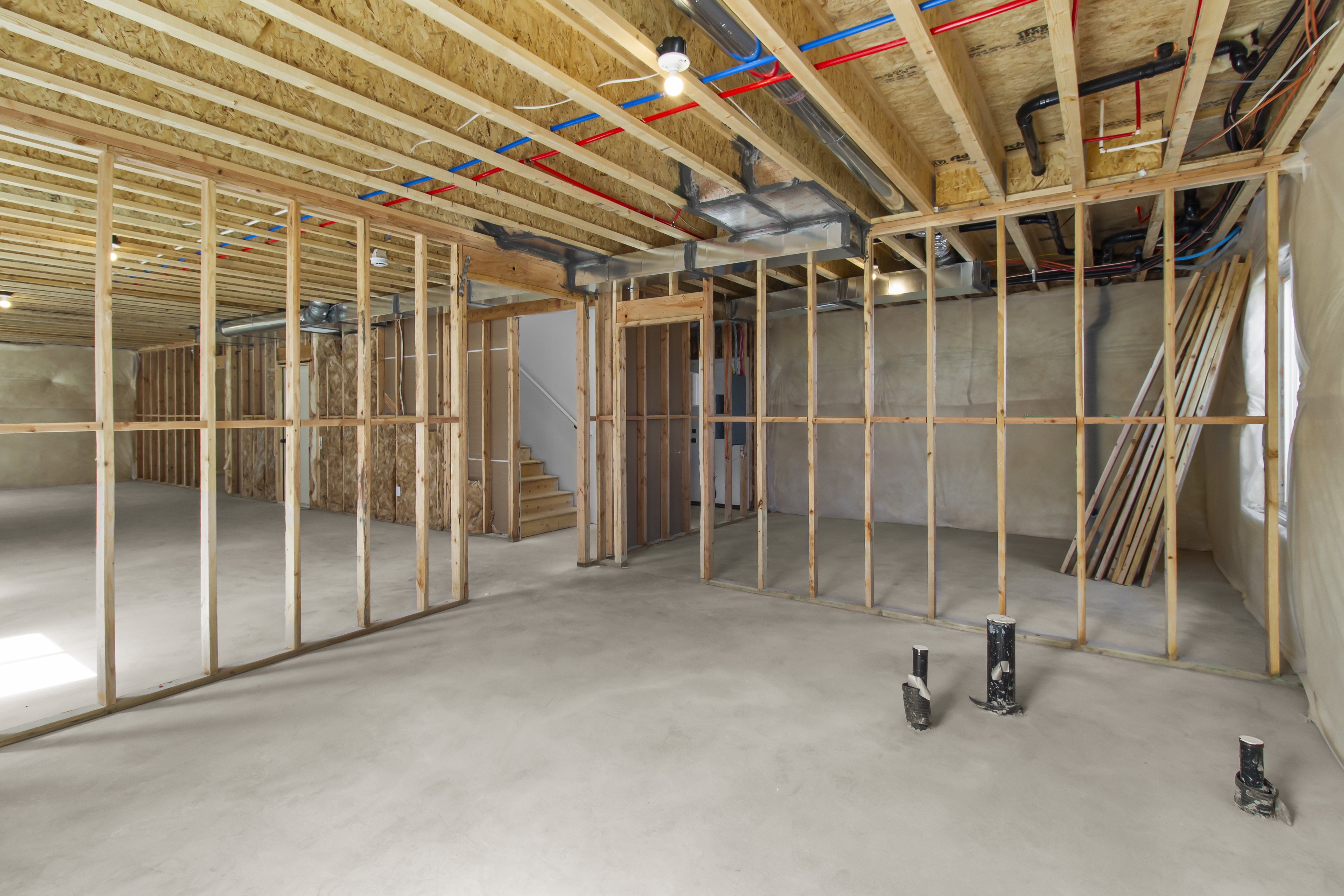 Unfinished basement featuring extensive framing, exposed ceiling joists, concrete flooring, visible PEX plumbing, and PVC drainage piping