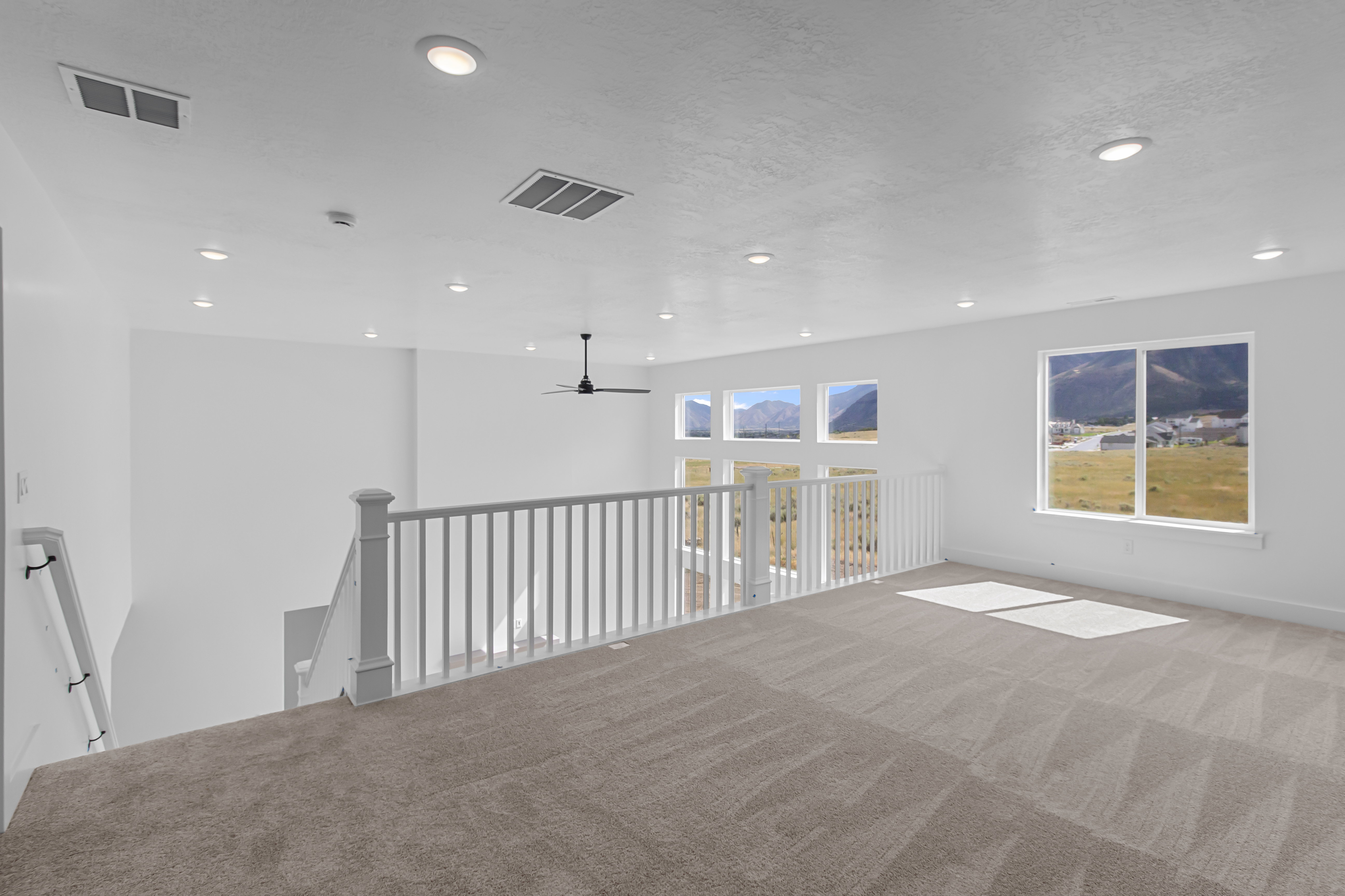 Spacious loft area featuring neutral-toned carpeting, white baluster railings, and recessed ceiling lighting