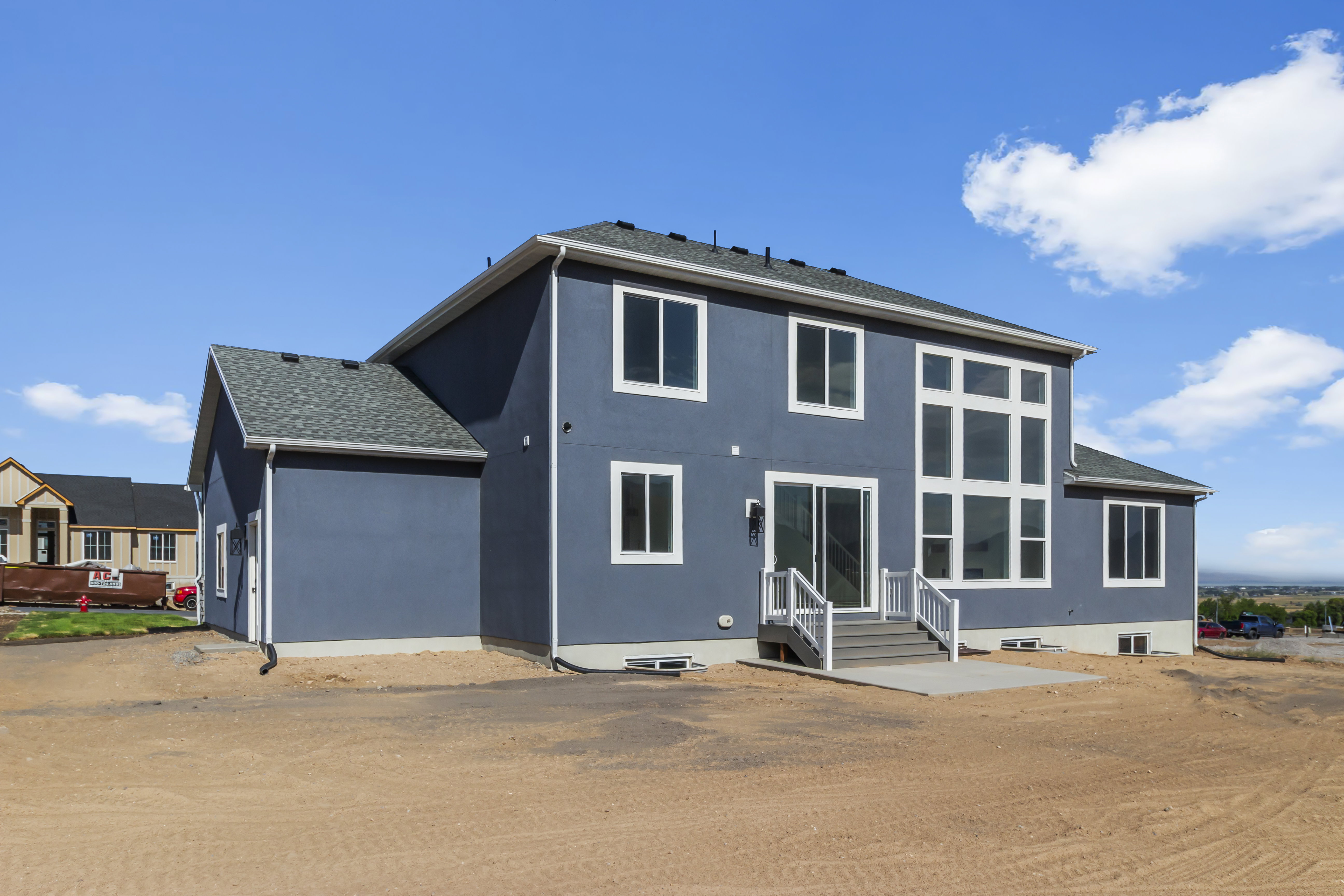 Contemporary exterior featuring a charcoal-hued facade, a multi-pane window wall, a concrete patio, a sliding glass door, and white trim accents