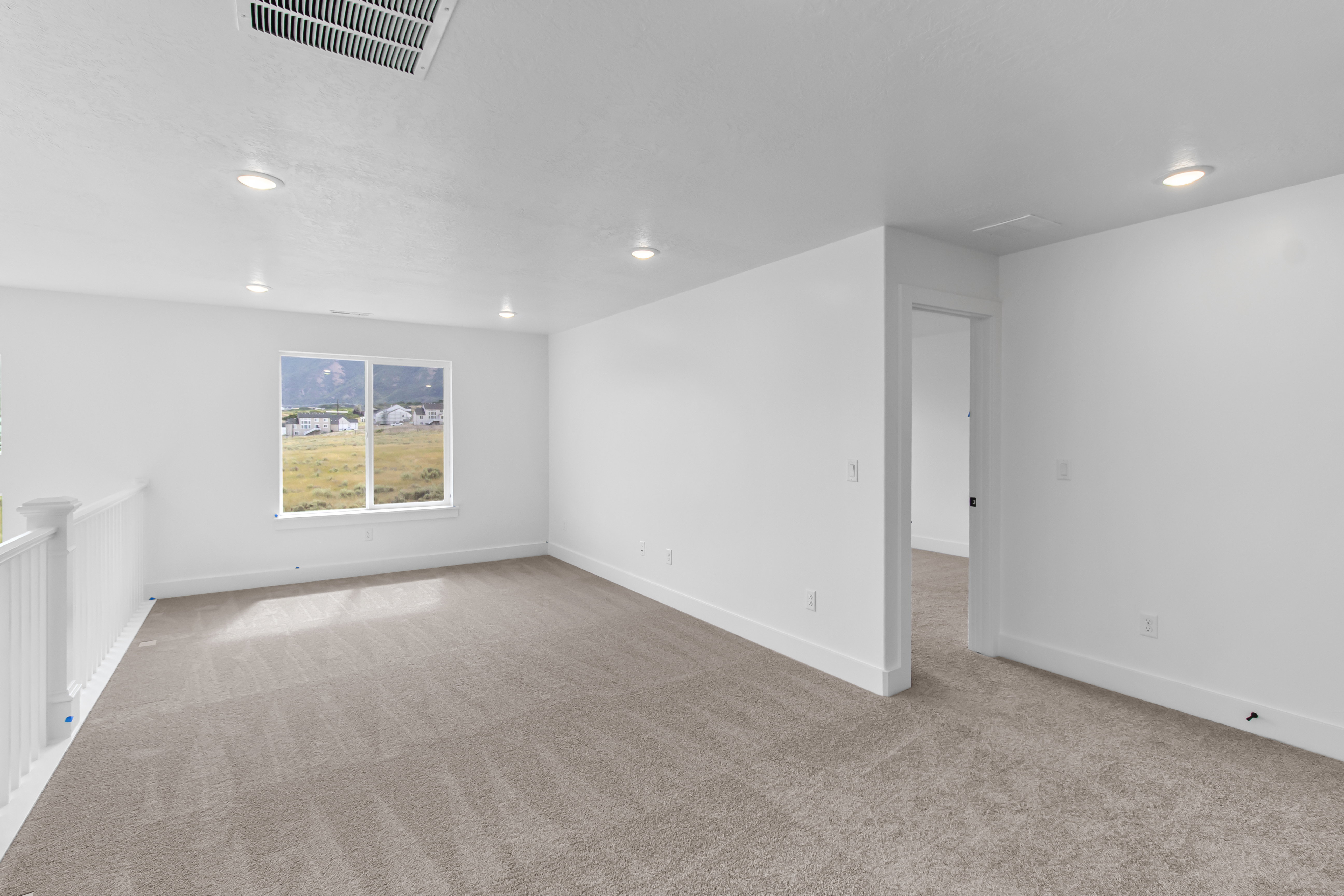 Spacious carpeted room featuring recessed lighting, a large window, white walls, and white baseboards
