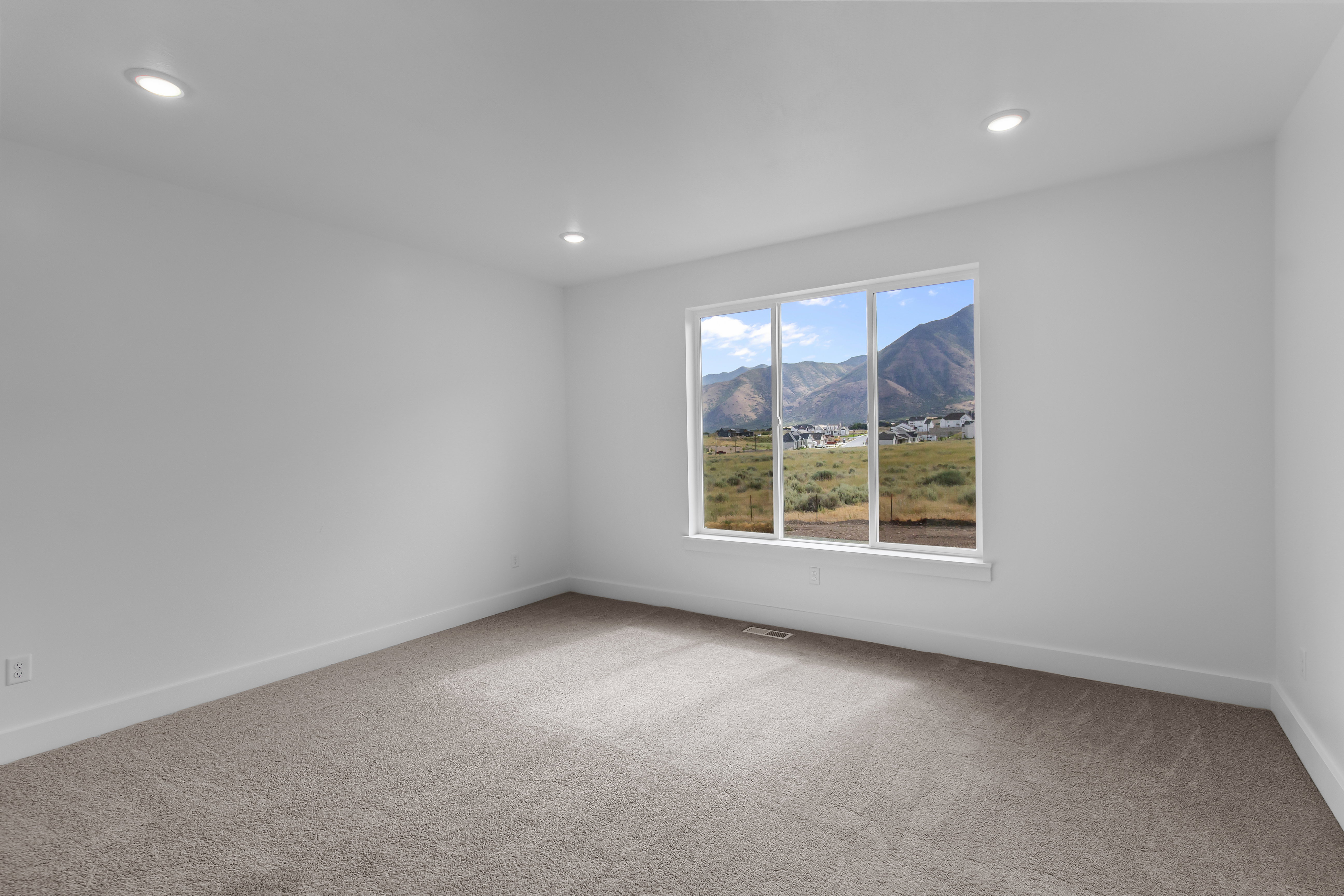 Spacious room featuring neutral carpeting, white walls, recessed ceiling lighting, and a large window offering mountain scenery